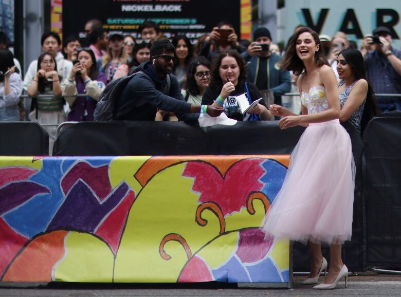 A woman in strapless pink knee-length dress signs autographs for fans outside a theatre during TIFF.