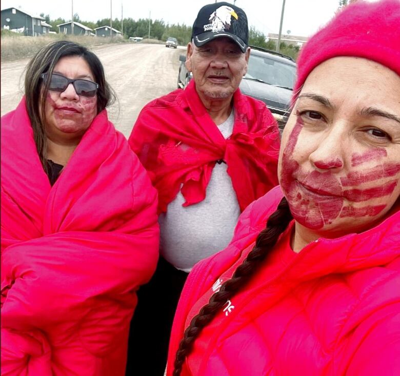 Three people wearing red clothing pose for a selfie on a gravel road.