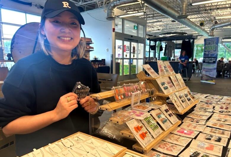 A woman wearing a black sweater and black hat sitting behind a table of merchandise. 