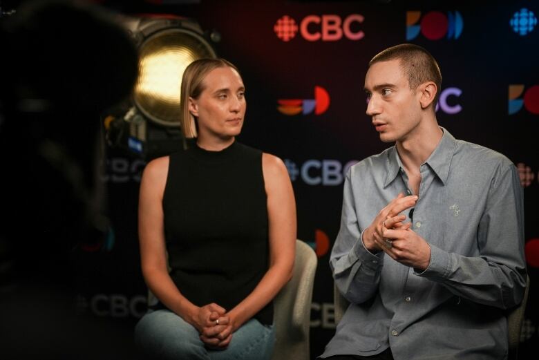 Two interview subjects sit side by side in front of a CBC themed background. 