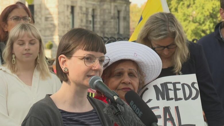 A woman wearing glasses speaks into a microphone.