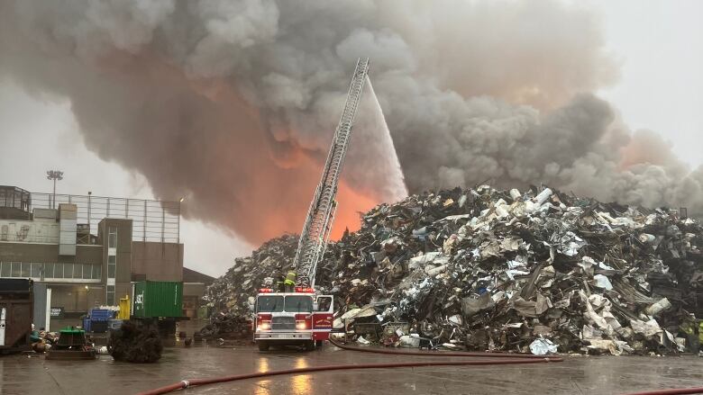 Smoke billowing out of a large pile of metal, fire truck pouring liquid onto it