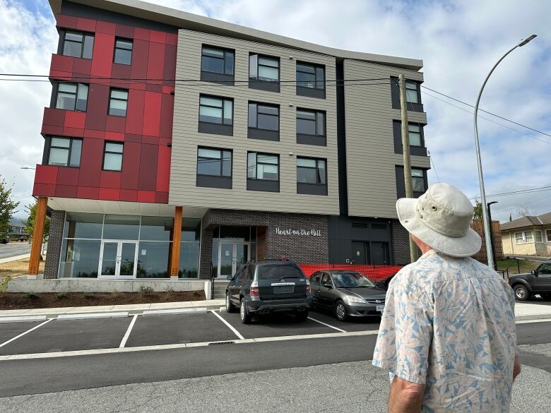 A man in a tilly hat looks up at a new, four-storey apartment building. 