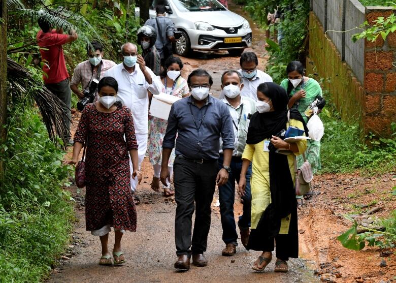 A group of men and women, all wearing medical masks, walking through a rural village.