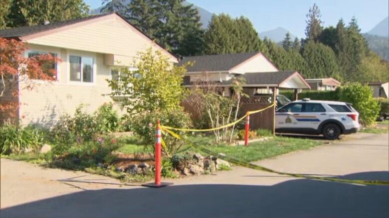 A one-storey home on a small street is behind police tape and an RCMP SUV is parked in a driveway next door.