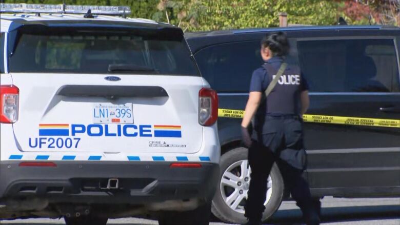 A police officer walks between a police SUV and a black van. The van has police tape wrapped around it.