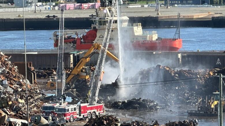 A smoking pile of scrap metal, fire trucks spraying water over it