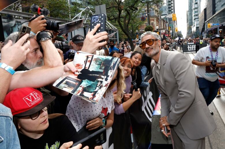 A man in designer sunglasses takes photos with fans behind a barricade at TIFF.