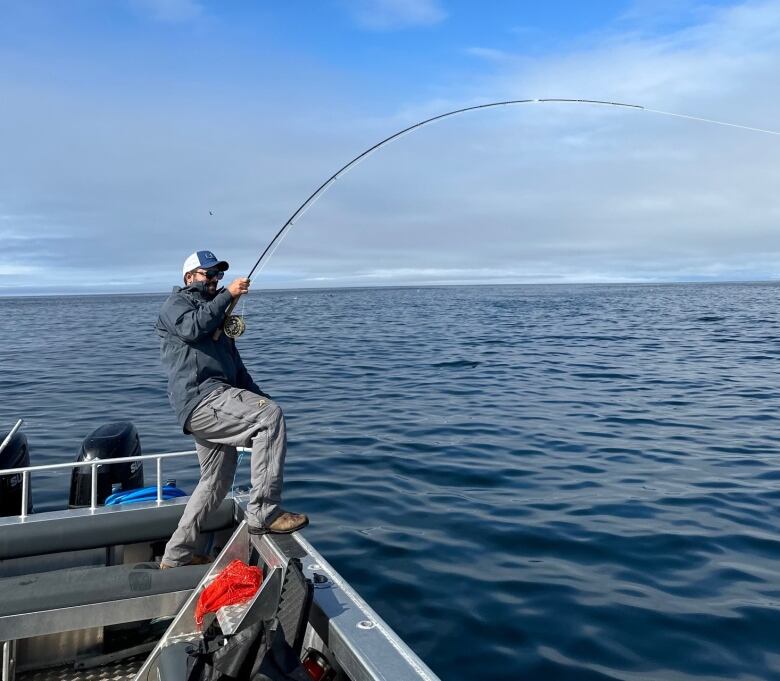 A man stands in a boat on the water, holding a fishing rod.