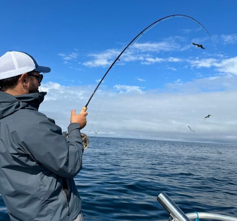 A man holds a curved fishing rod over the water.