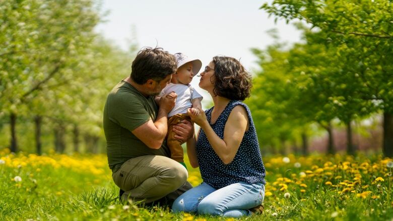 Parents hold their child in an apple orchard.