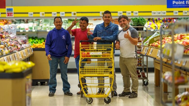 Four men pose for a photo with a cart in a grocery store's produce section.