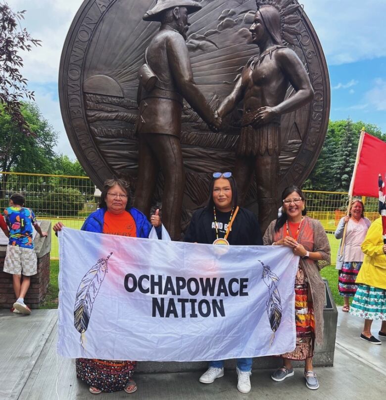 A group of Indigenous people hold up a white flag with black lettering of Ochapowace Nation 