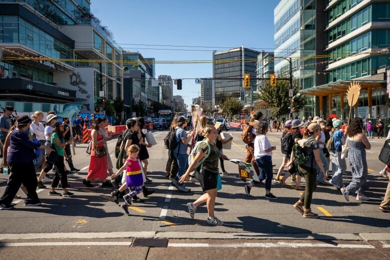 A line of people with signs are crossing a busy intersection. 