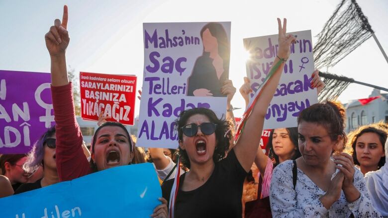 Women hold signs and shout.