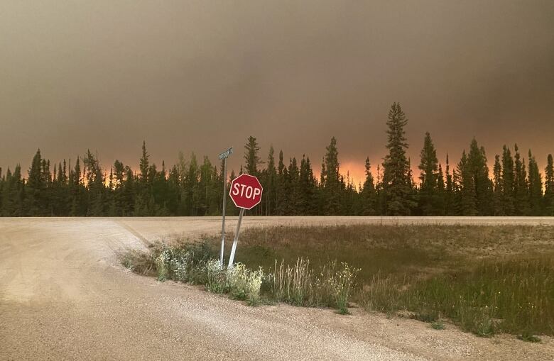 An orange and smoky sky seen over a stop sign near a rural highway intersection.