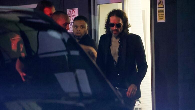 A man with sunglasses on walks to a car at night.