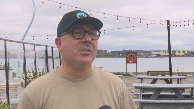 A man in a beige t-shirt speaks to the camera.