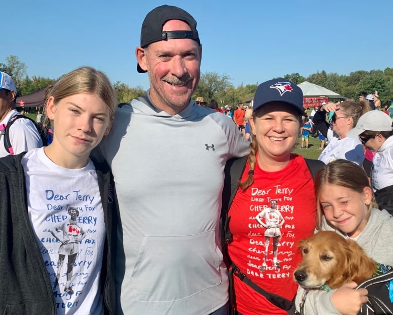 A man and a woman in sportswear pose with their teenage daughters and dog.