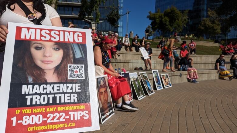 a close-up shot of a photograph of a missing woman with people milling in the background