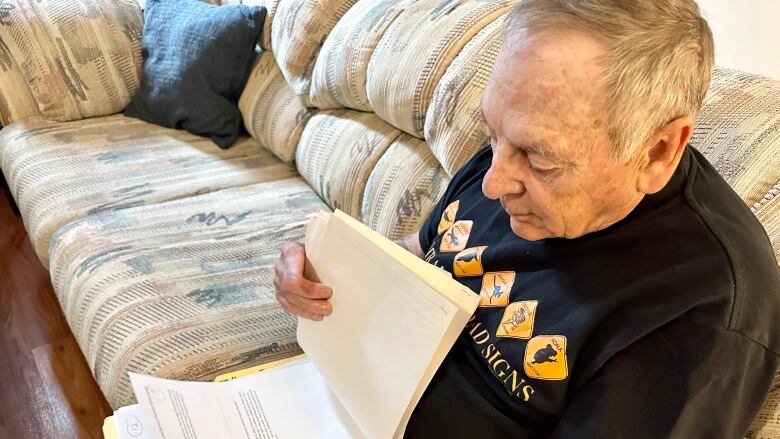 A senior age man on a couch looks through a folder of papers.