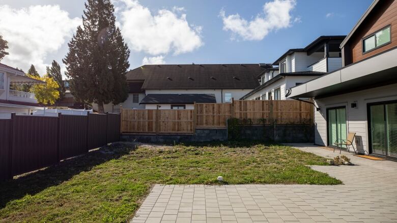 A green but barren backyard is pictured next to a new house with wood paneling.