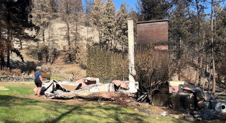 A woman looks at the burned out remains of her home that is destroyed after a fire right down to the concrete foundations.