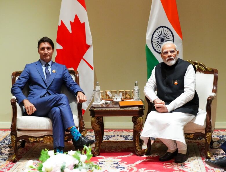 Two men sitting in ornate chairs, with flags of their respective countries behind them.