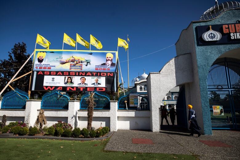 People entering a gurdwara in Surrey, B.C., with a giant poster by its entrance featuring two slain Sikh men and below them photoss of three other people from the High Commission of India and it reads: assassination wanted.