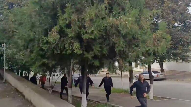 Several people appear to be running down a tree-lined sidewalk in an urban setting.