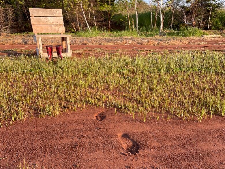 Footsteps are seen in sand, with a chair and rubber boots in the background.