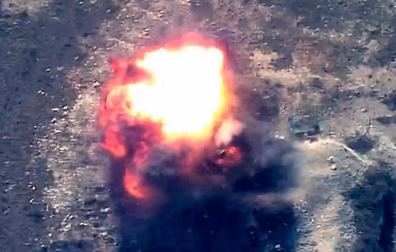 A large explosion is shown in a rural valley.