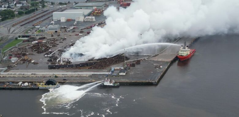 A huge arc of water is shot from a large vessel onto a pile of scrap on fire at a waterside dock.