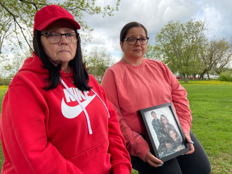 Laurie Brooks and Amy Paul sit holding a photo of Erin Brooks and two children.