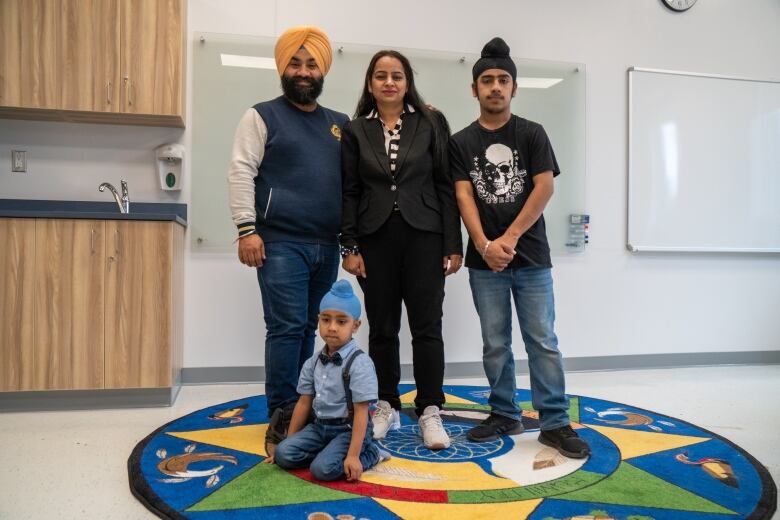 A family poses for a photo, standing on a multi-coloured mat in a classroom.