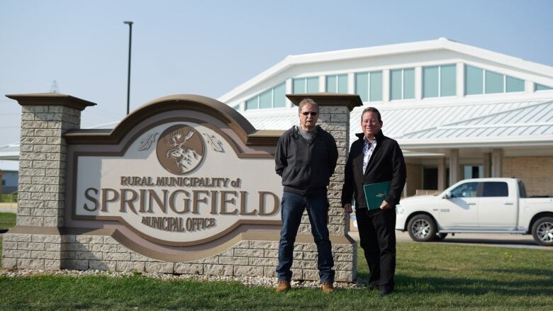 Two politicians stand next to a sign that reads 'Rural Municipality of Springfield Municipal Office.'