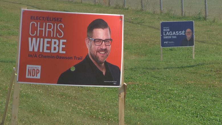 A orange election sign and a blue election sign are pictured in a ditch.