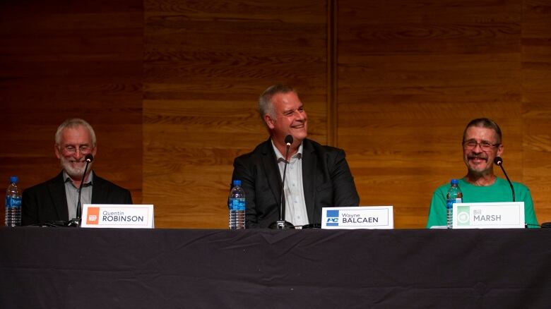 Three men sit smiling at a table.