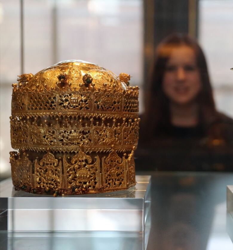 A employee poses in front of a Crown (L), made in Ethiopia around 1740, made of gold and gilded copper with glass beads, pigment and fabric and a gold chalise, made by Walda Giyorgis in Gondar, Ethiopia between 1735 and 1740 at an exhibition, 