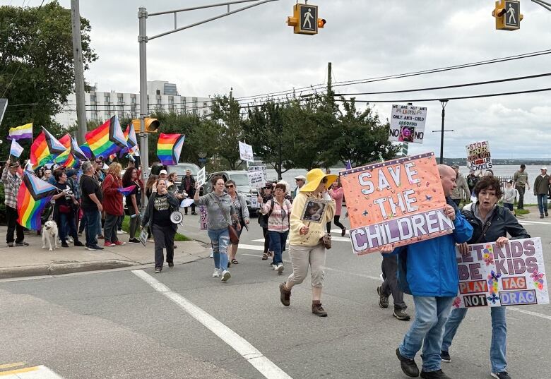 Groups of people with signs and rainbow flags are shown at a street corner.