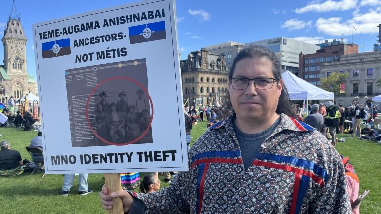 A man in a ribbon short holding a sign at a demonstration.