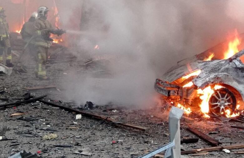 Firefighters use a hose to spray water on a burning car and other debris