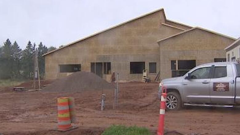 A building under construction, surrounded by piles of dirt and orange construction cones. 