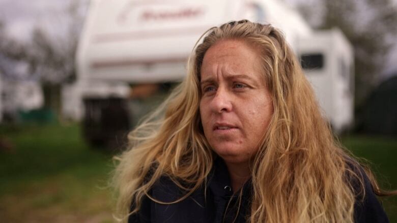 A woman looks concerned sitting in front of a camper. 