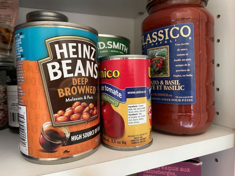 Canned baked beans and a jar of pasta sauce on a shelf.