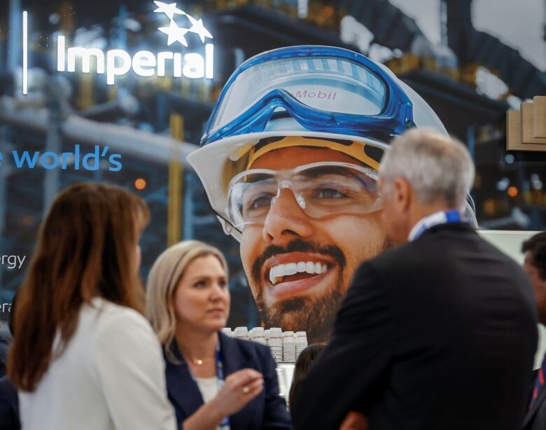 Delegates chat in front of an image of oil workers at the World Petroleum Congress  in Calgary, Monday, Sept. 18, 2023.THE CANADIAN PRESS/