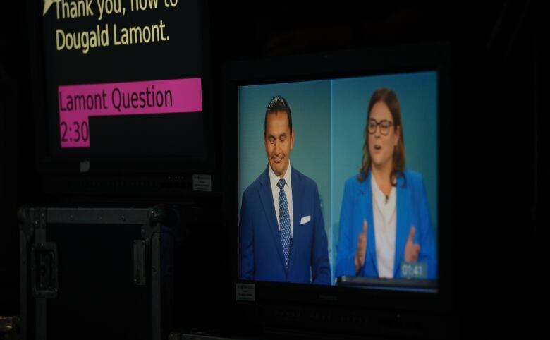 Two people in business attire are shown on the screen of a camera with prompter directions in the foreground.