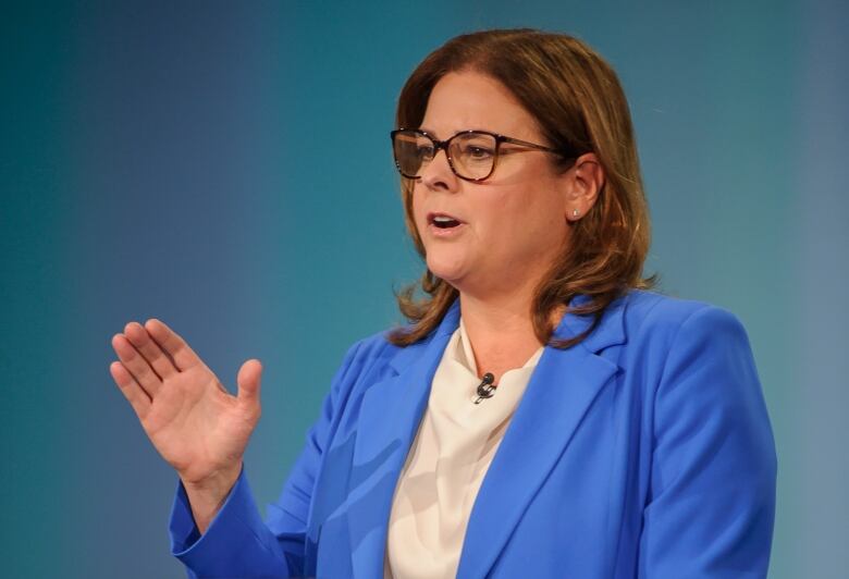 A woman in a suit speaks at a podium.