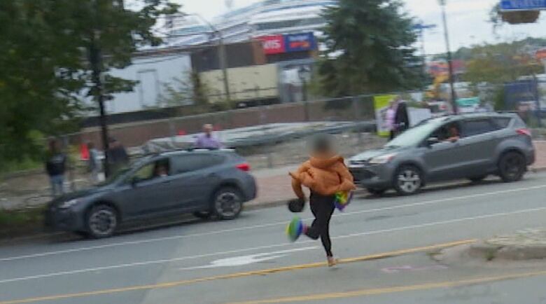 A person running across a street carrying a pride flag.