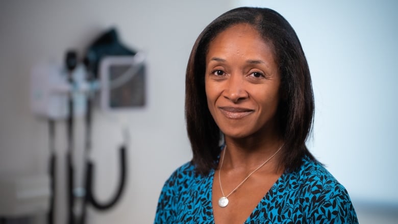 Female family doctor stands in an examining room.